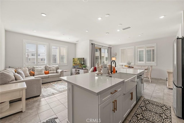 kitchen with a kitchen island with sink, sink, light tile patterned flooring, and appliances with stainless steel finishes