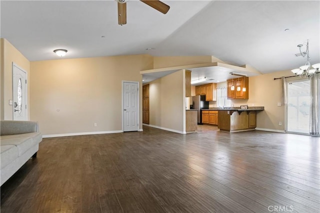 unfurnished living room featuring vaulted ceiling, ceiling fan with notable chandelier, and dark hardwood / wood-style floors