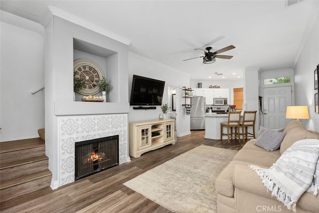 living room with dark hardwood / wood-style floors, ceiling fan, ornamental molding, and a tiled fireplace