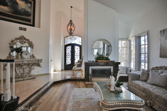 living room with hardwood / wood-style floors, high vaulted ceiling, french doors, a fireplace, and a notable chandelier