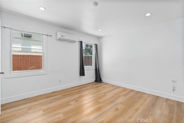 unfurnished room with a wall unit AC and light hardwood / wood-style floors