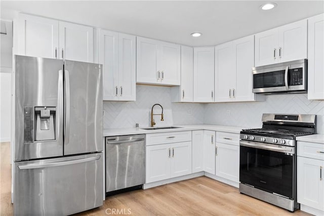 kitchen with stainless steel appliances, sink, white cabinetry, light hardwood / wood-style flooring, and decorative backsplash