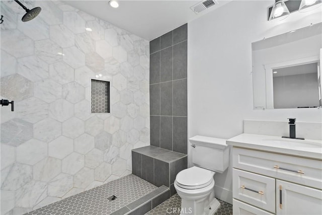 bathroom featuring toilet, tiled shower, tile patterned flooring, and vanity