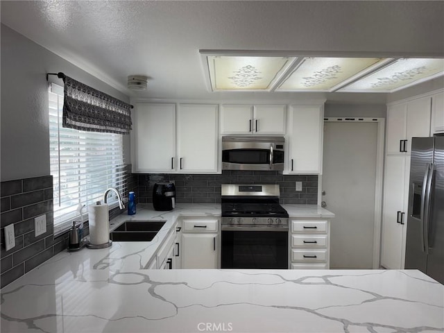 kitchen with white cabinets, sink, decorative backsplash, light stone counters, and stainless steel appliances