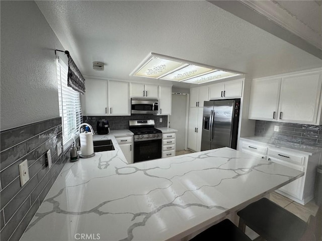 kitchen featuring sink, stainless steel appliances, backsplash, kitchen peninsula, and white cabinets