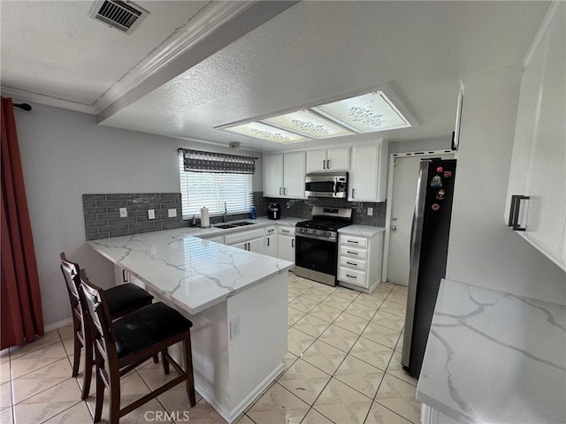 kitchen with white cabinets, sink, decorative backsplash, appliances with stainless steel finishes, and kitchen peninsula