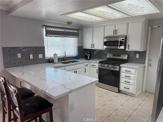 kitchen featuring kitchen peninsula, appliances with stainless steel finishes, backsplash, white cabinets, and a breakfast bar area