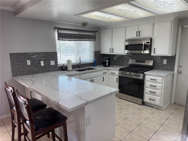 kitchen featuring kitchen peninsula, light stone counters, stainless steel appliances, sink, and white cabinets