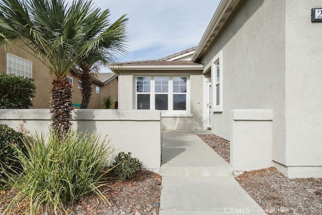 view of exterior entry with fence and stucco siding