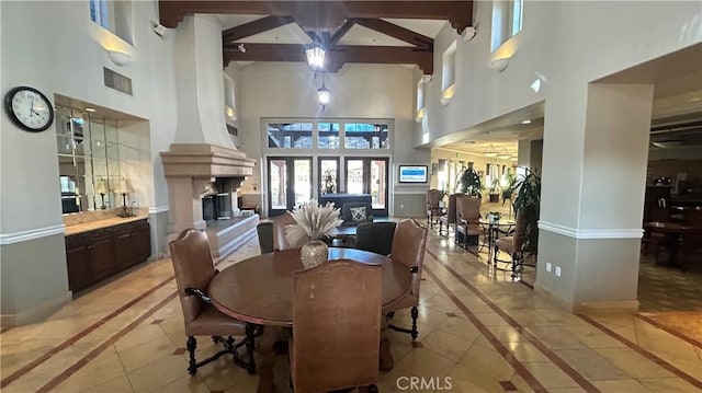 dining room with a large fireplace, visible vents, baseboards, a high ceiling, and beam ceiling