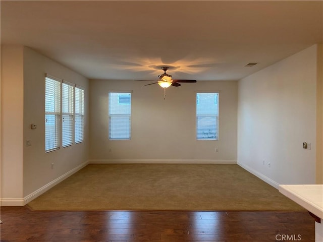 empty room featuring wood-type flooring, visible vents, baseboards, and ceiling fan