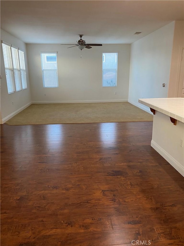 empty room featuring ceiling fan, dark wood-type flooring, visible vents, and baseboards