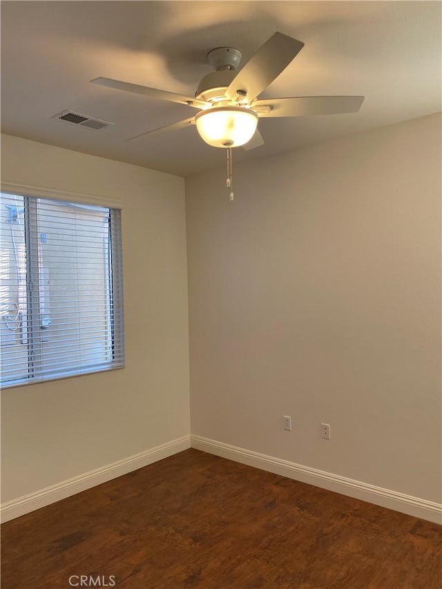 spare room featuring dark wood-style floors, ceiling fan, visible vents, and baseboards