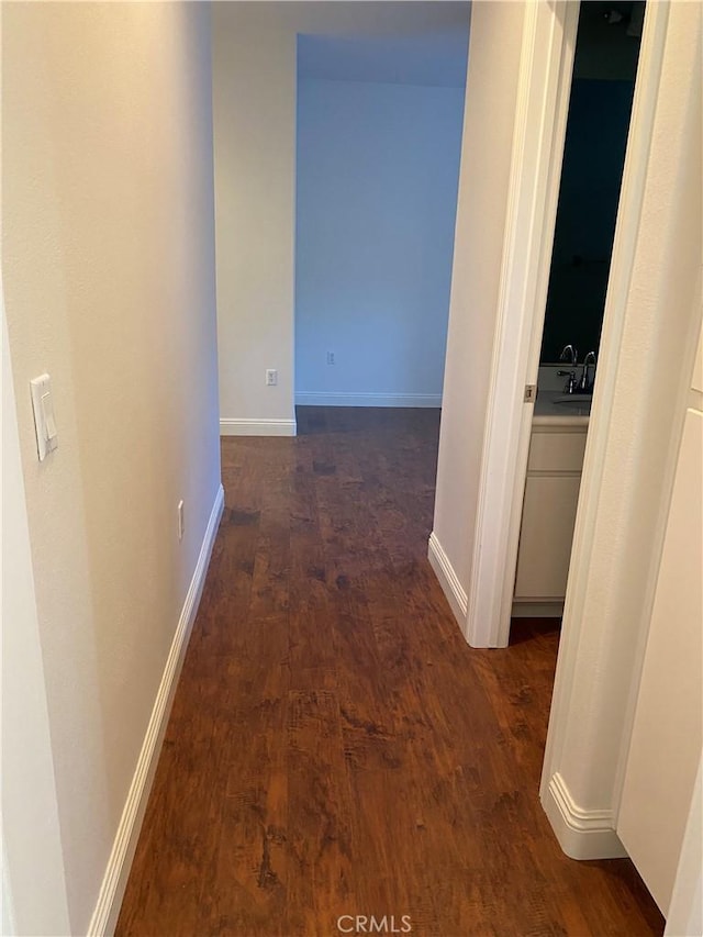 corridor featuring dark wood-style flooring, a sink, and baseboards