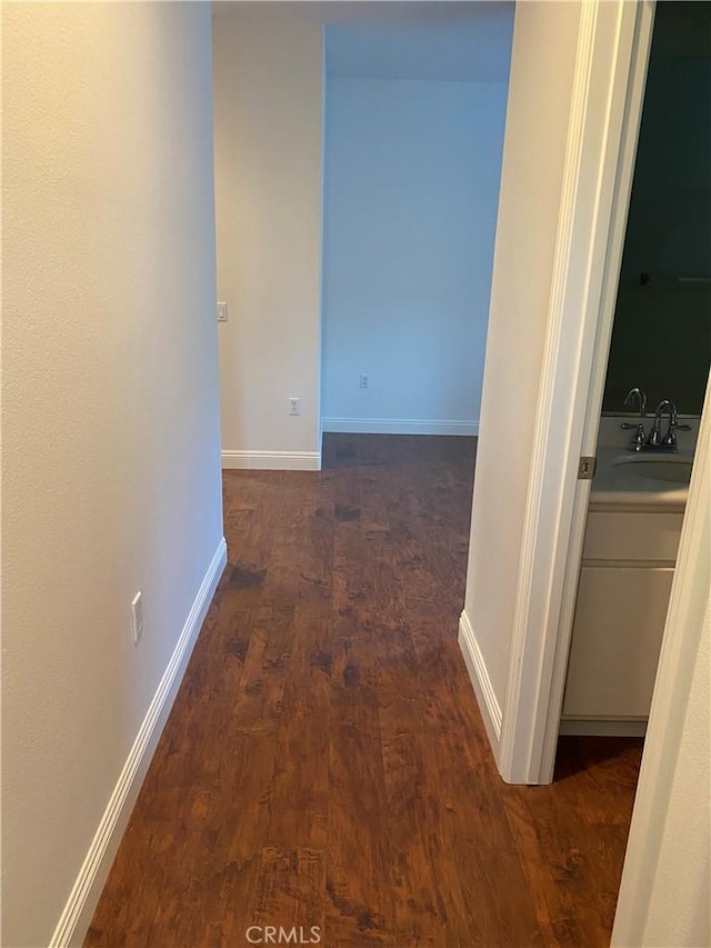 corridor featuring wood finished floors, a sink, and baseboards