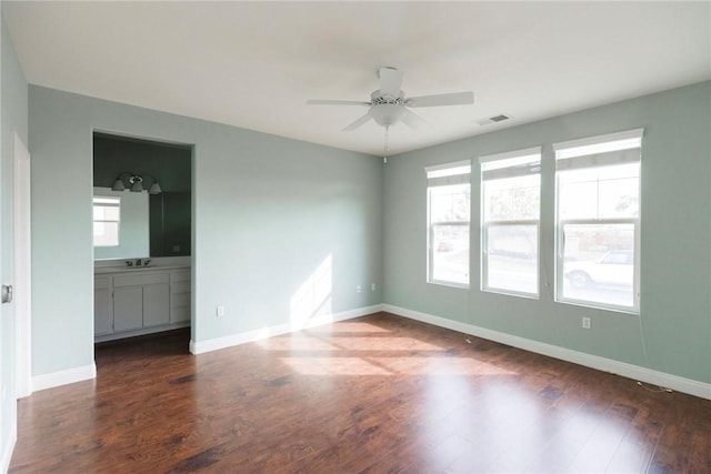 empty room with visible vents, dark wood-type flooring, ceiling fan, a sink, and baseboards