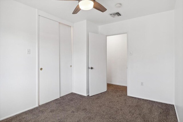 unfurnished bedroom with ceiling fan, a closet, and dark carpet