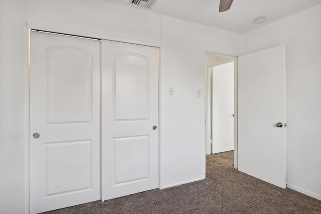 unfurnished bedroom with dark colored carpet, ceiling fan, and a closet