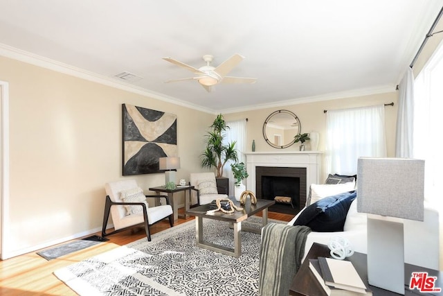 living room with wood-type flooring, a brick fireplace, ceiling fan, and crown molding