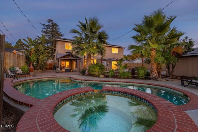 pool at dusk featuring an in ground hot tub and a patio area