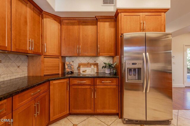 kitchen with decorative backsplash, stainless steel fridge with ice dispenser, light tile patterned flooring, and dark stone counters