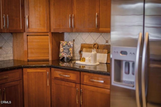 kitchen with stainless steel fridge with ice dispenser, backsplash, and dark stone counters