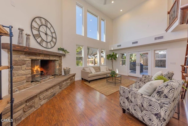 living room featuring a stone fireplace, french doors, a towering ceiling, and wood-type flooring