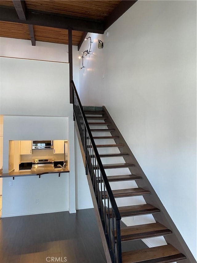 staircase with beam ceiling, a towering ceiling, wood ceiling, and hardwood / wood-style flooring