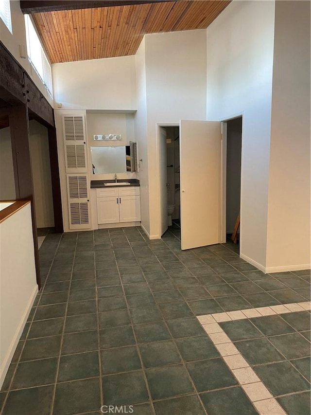 unfurnished living room with sink, a towering ceiling, dark tile patterned flooring, and wood ceiling