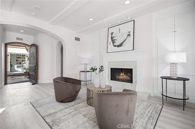 living room with beam ceiling, a premium fireplace, and light hardwood / wood-style floors