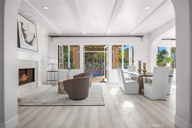 living room with beamed ceiling, a high end fireplace, and light hardwood / wood-style flooring