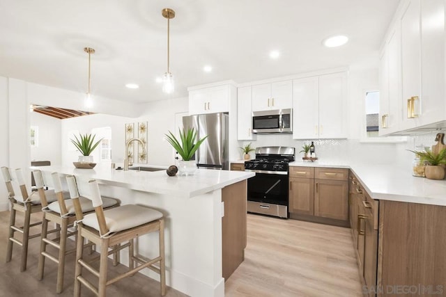 kitchen with light wood-type flooring, appliances with stainless steel finishes, decorative light fixtures, white cabinetry, and a breakfast bar area