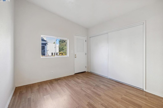 unfurnished bedroom with light hardwood / wood-style floors, lofted ceiling, and a closet