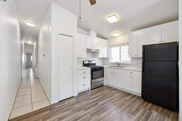 kitchen featuring black refrigerator, white cabinets, stainless steel range with gas cooktop, and sink