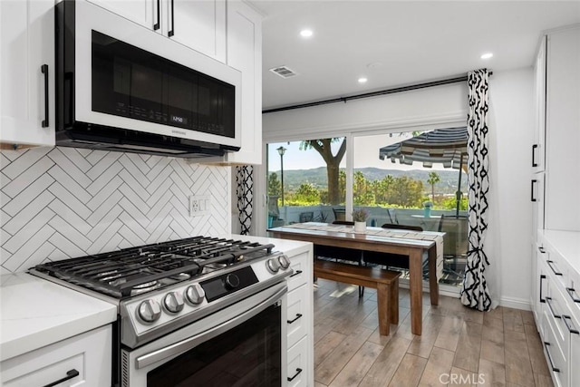 kitchen featuring decorative backsplash, stainless steel range with gas cooktop, white cabinets, and light hardwood / wood-style flooring