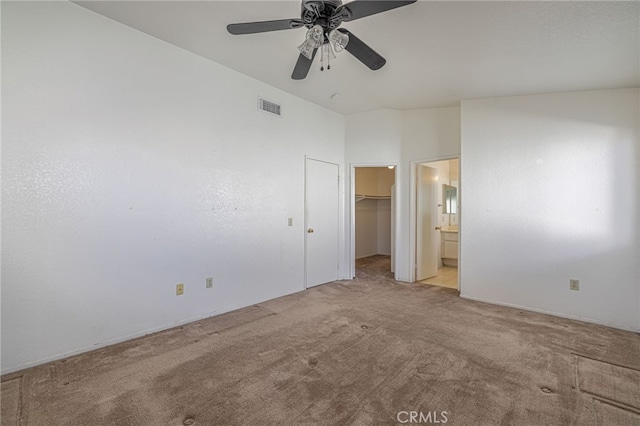 unfurnished bedroom with a walk in closet, ensuite bath, light colored carpet, ceiling fan, and a closet