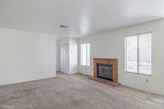 unfurnished living room featuring light colored carpet, a textured ceiling, a wealth of natural light, and a brick fireplace