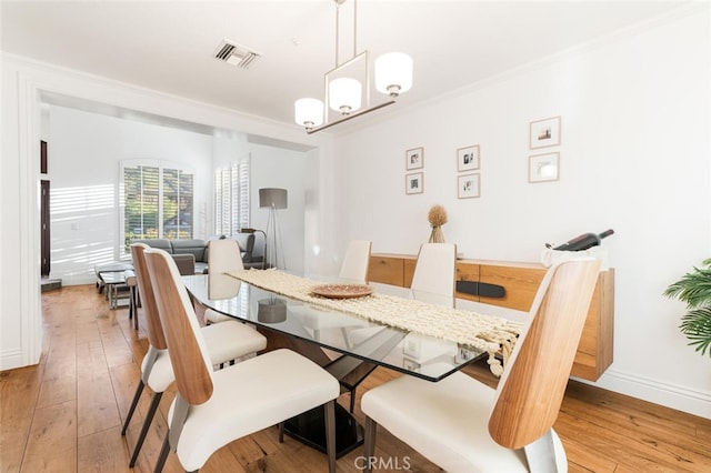 dining area featuring crown molding, light hardwood / wood-style flooring, and an inviting chandelier