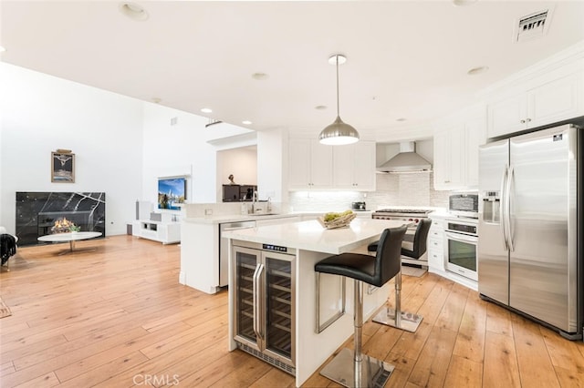 kitchen with hanging light fixtures, wall chimney range hood, kitchen peninsula, a kitchen bar, and appliances with stainless steel finishes