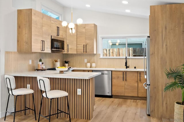 kitchen featuring a breakfast bar, vaulted ceiling, light hardwood / wood-style floors, kitchen peninsula, and stainless steel appliances