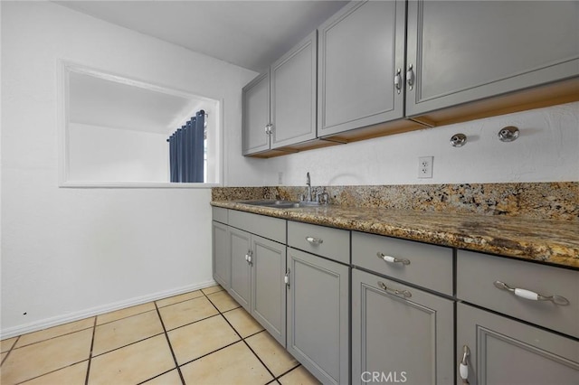 kitchen with light tile patterned floors, gray cabinets, dark stone countertops, and sink