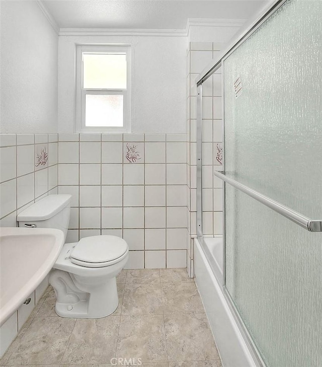 bathroom featuring crown molding, toilet, shower / bath combination with glass door, and tile walls