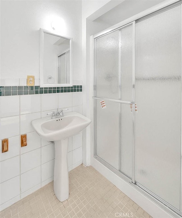 bathroom with tile patterned floors, a shower with door, tile walls, and sink