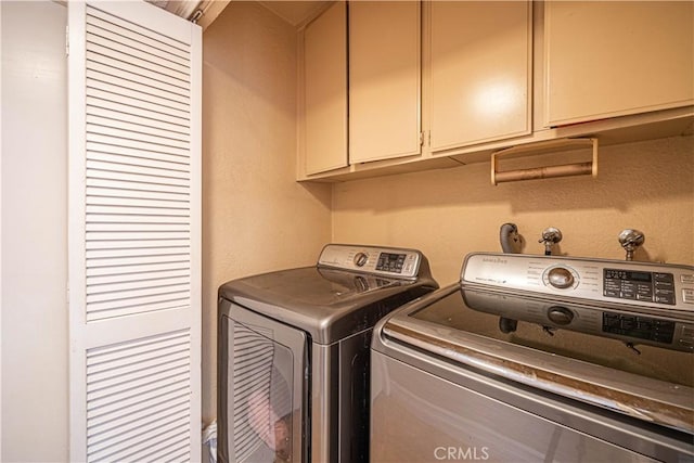 clothes washing area with washer and clothes dryer and cabinets