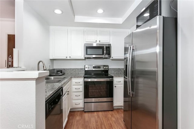 kitchen with white cabinetry, stainless steel appliances, kitchen peninsula, light hardwood / wood-style floors, and a tray ceiling