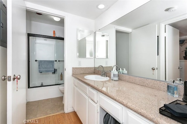 full bathroom featuring hardwood / wood-style flooring, vanity, toilet, and combined bath / shower with glass door