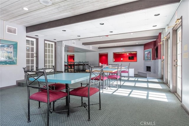 carpeted dining area featuring beamed ceiling, a brick fireplace, and plenty of natural light