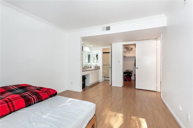 bedroom featuring ensuite bath, crown molding, a walk in closet, a closet, and light wood-type flooring