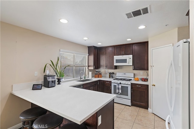 kitchen with white appliances, a kitchen bar, sink, kitchen peninsula, and light tile patterned floors