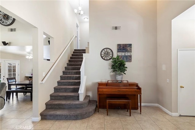 staircase featuring ceiling fan with notable chandelier, a high ceiling, tile patterned floors, and french doors